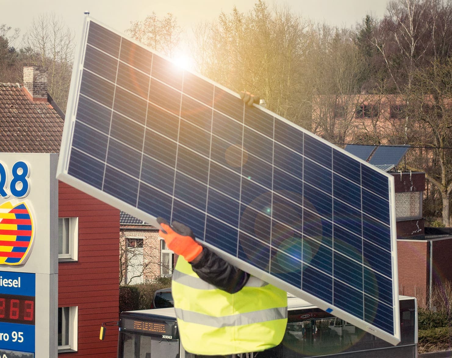 A worker lifting a solar panel into place beside a Q8 service station price sign.