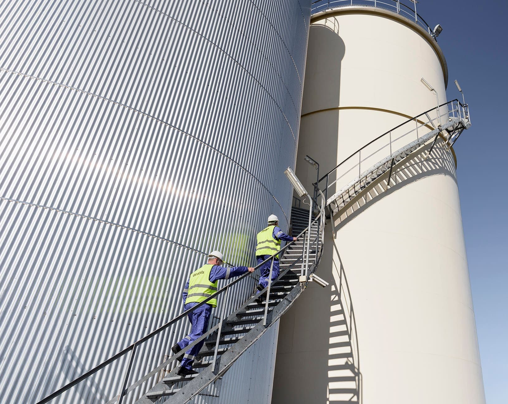 Two workers climbing the outside stairs of a storage tank.